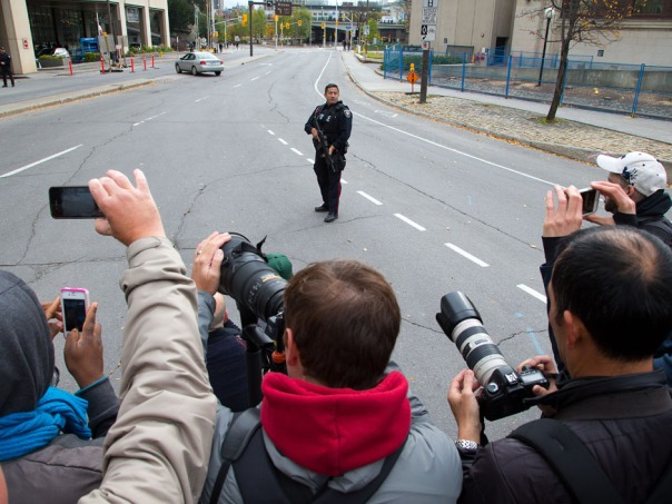 An employee of the Ottawa police department points his firearm at Canadian citizens. 